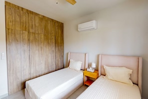 Ein Hotelzimmer mit zwei Betten, einem Holzschrank, einem Nachttisch mit Lampe und einer Klimaanlage.