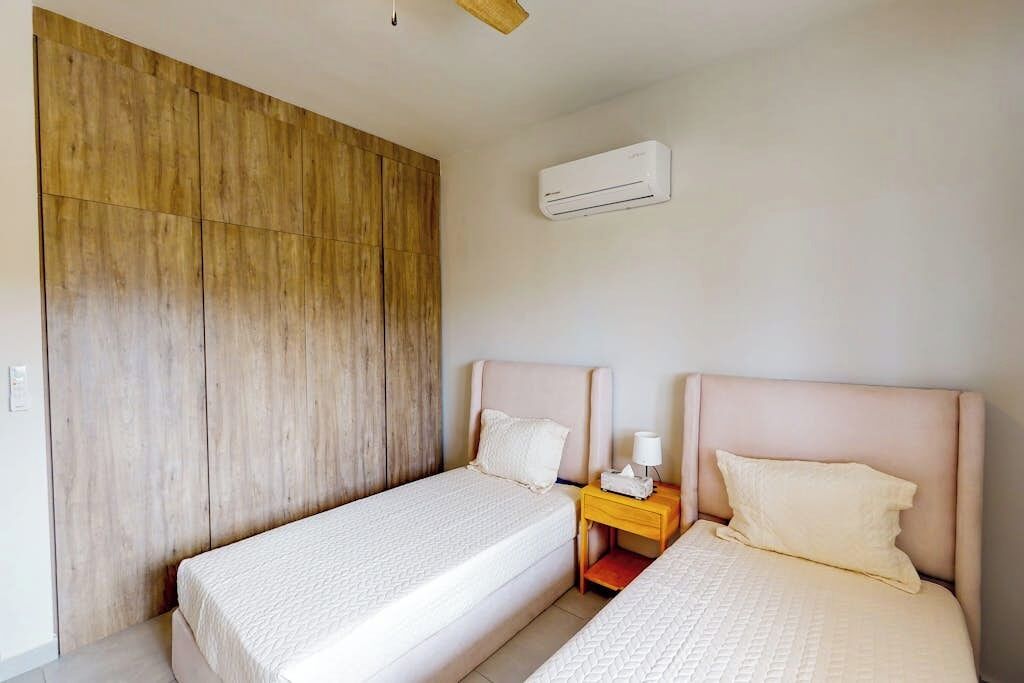 Ein Schlafzimmer mit zwei Betten, einem Holzschrank, einem Nachttisch mit Lampe und einer Klimaanlage.