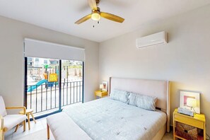 Ein Schlafzimmer mit einem Bett, einem Deckenventilator, einem Nachttisch, einem Sessel und Blick auf einen Spielplatz im Freien.