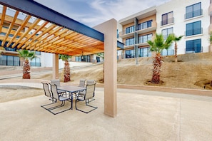 An outdoor patio with a wooden pergola, a table with chairs, and palm trees. - Gorgeous Dog-friendly Apartment With Balcony, Open Layout, Heated Pool, & AC (Cabo San Lucas)