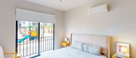 A bedroom with a bed, a nightstand, a chair, a ceiling fan, and a view of a playground through a sliding door.