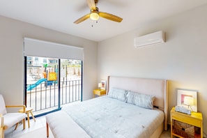 A bedroom with a bed, a nightstand, a chair, a ceiling fan, and a view of a playground through a sliding door. - Gorgeous Dog-friendly Apartment With Balcony, Open Layout, Heated Pool, & AC (Cabo San Lucas)
