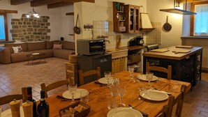 A cozy kitchen with a dining table set for four, a sofa in the living area, and a stone wall. - Exclusive Holiday Villa With Private Pool Between Marche and Umbria (Apecchio)