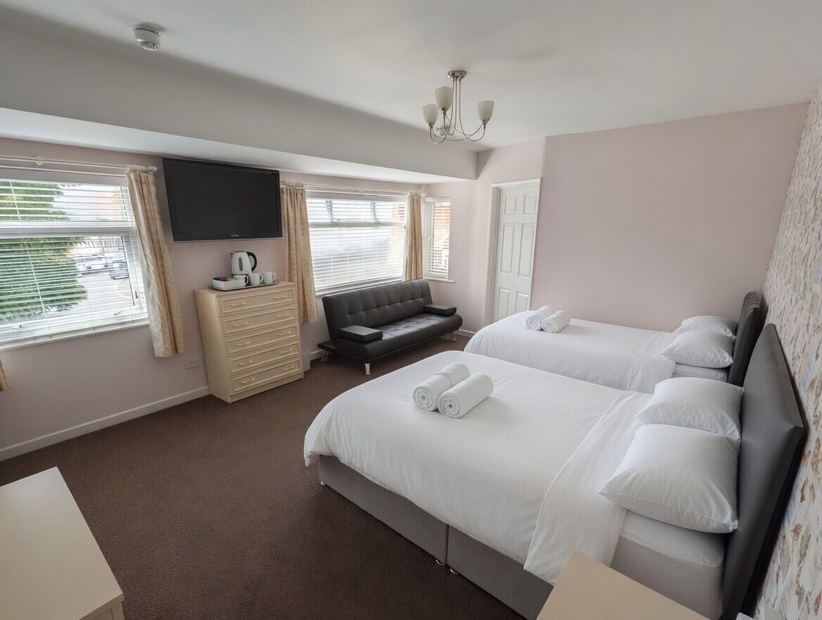 A hotel room with two beds, a TV, a sofa, and a dresser.