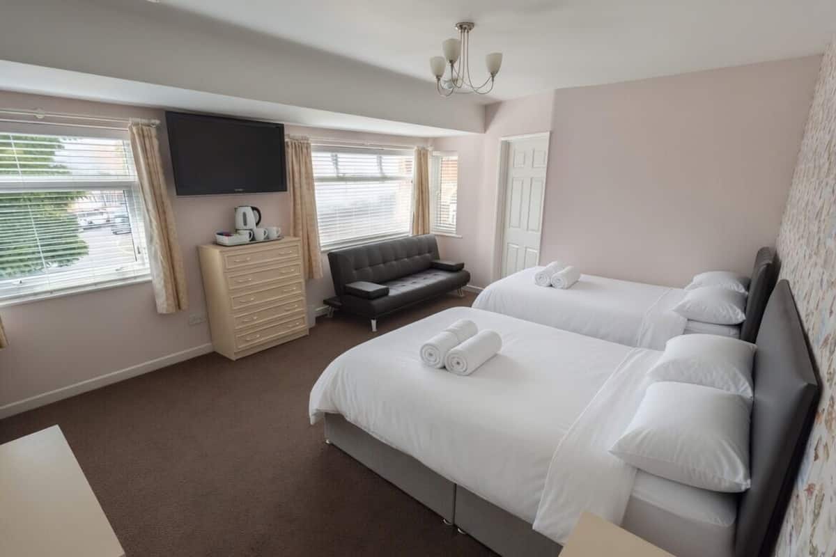 A hotel room with two beds, a TV, a sofa, and a dresser.