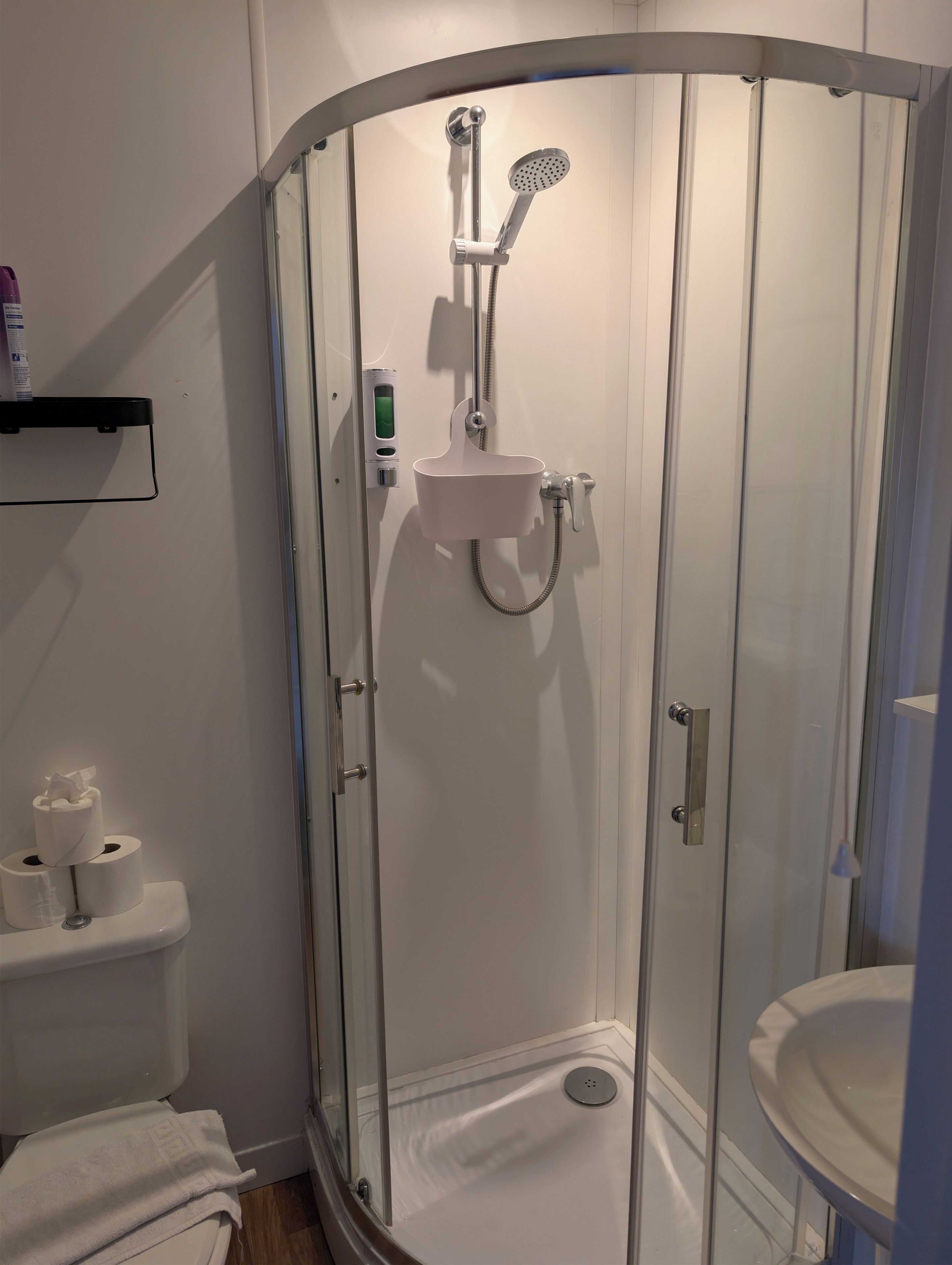 A modern bathroom with a glass-enclosed shower, a toilet with toilet paper, and a sink.