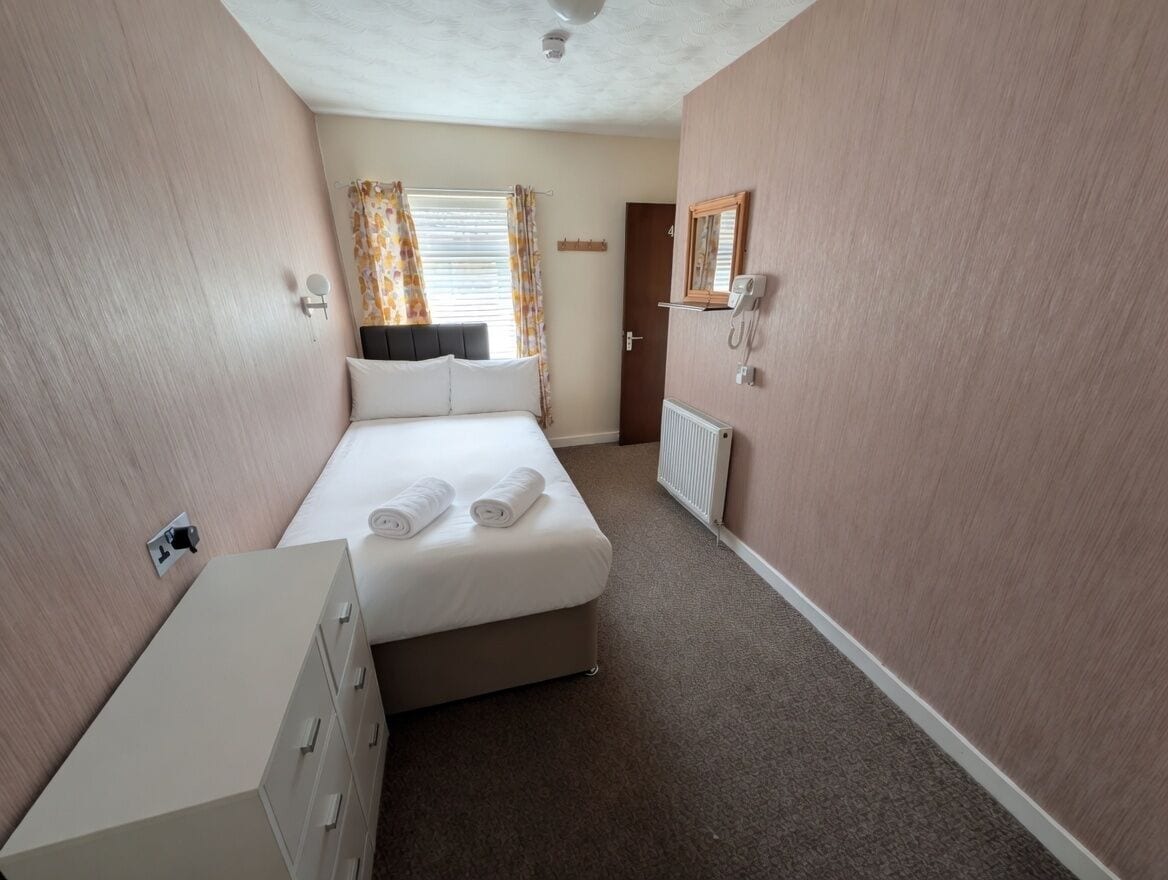 A bedroom with a bed, a dresser, a radiator, a telephone, and a door.