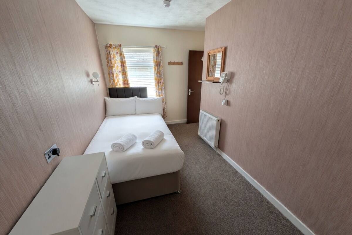A bedroom with a bed, a dresser, a radiator, a telephone, and a door.