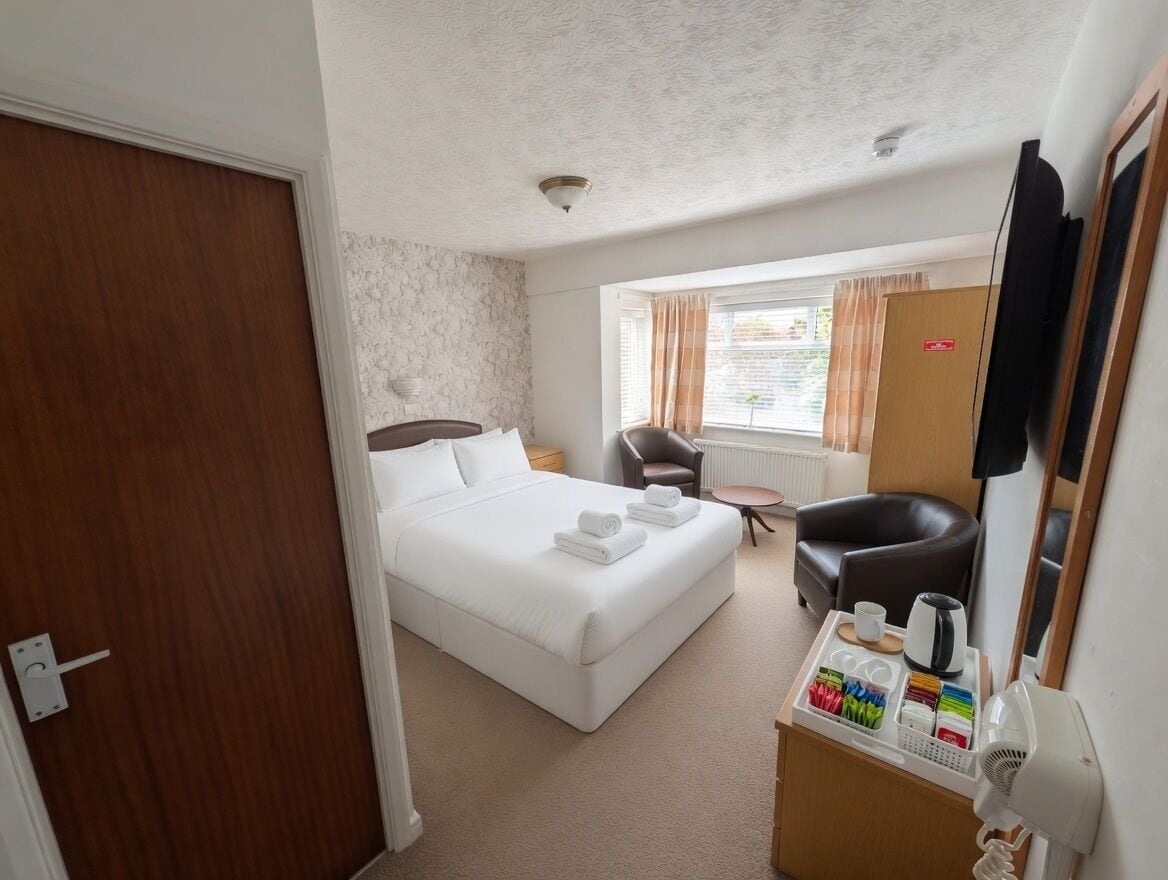 A hotel room with a bed, a desk with a hairdryer, a chair, and a television.