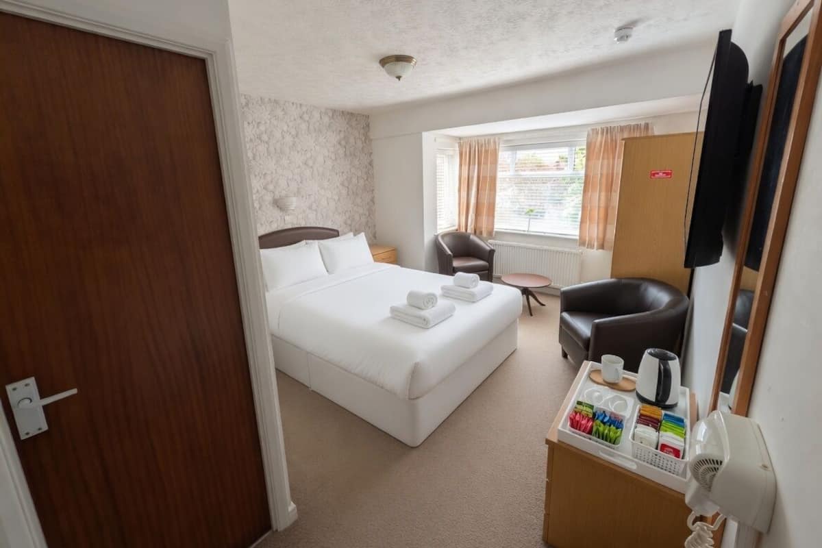 A hotel room with a bed, a desk with a hairdryer, a chair, and a television.