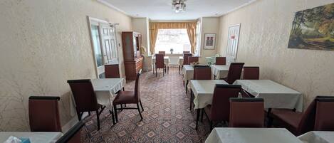 A hotel dining area with tables, chairs, patterned carpet, and a painting on the wall.