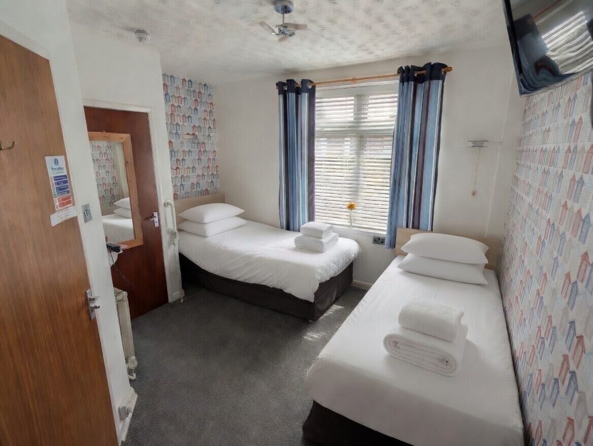 A hotel room with two beds, a ceiling fan, a window with curtains, and a patterned wall.