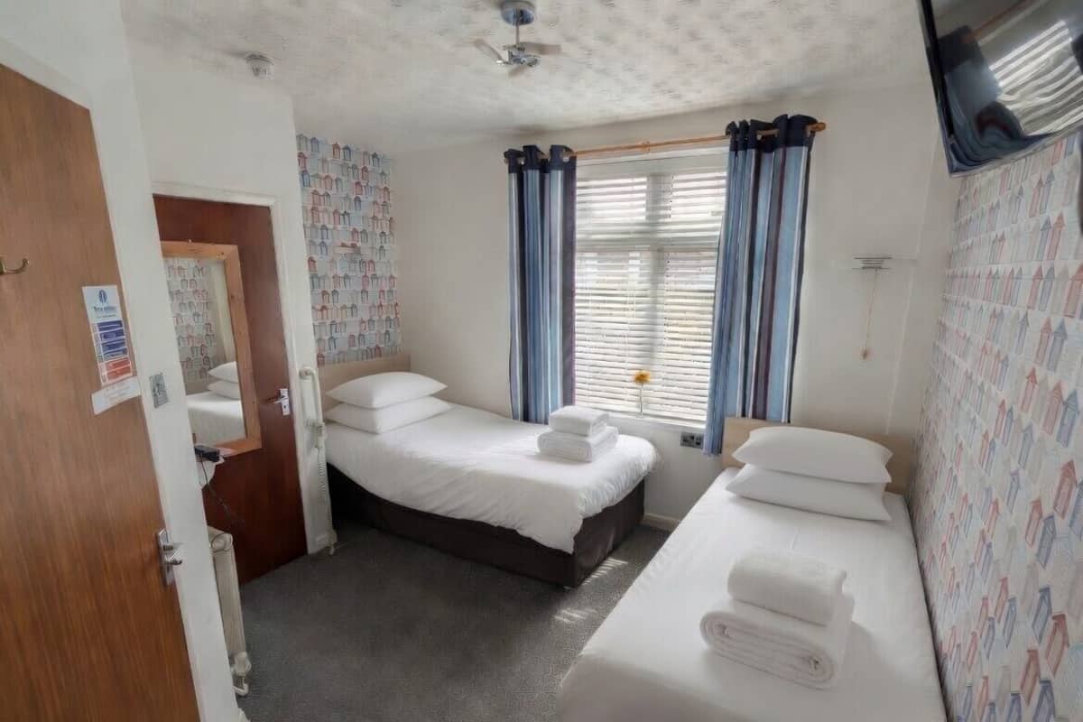 A hotel room with two beds, a ceiling fan, a window with curtains, and a patterned wall.