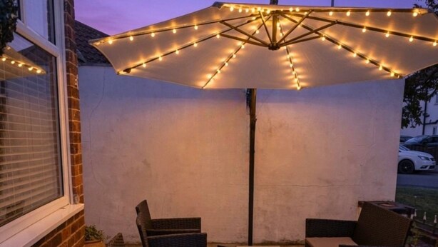 An outdoor patio with wicker furniture, a table, and a string-lit umbrella. - Mayfair Hotel (Skegness)