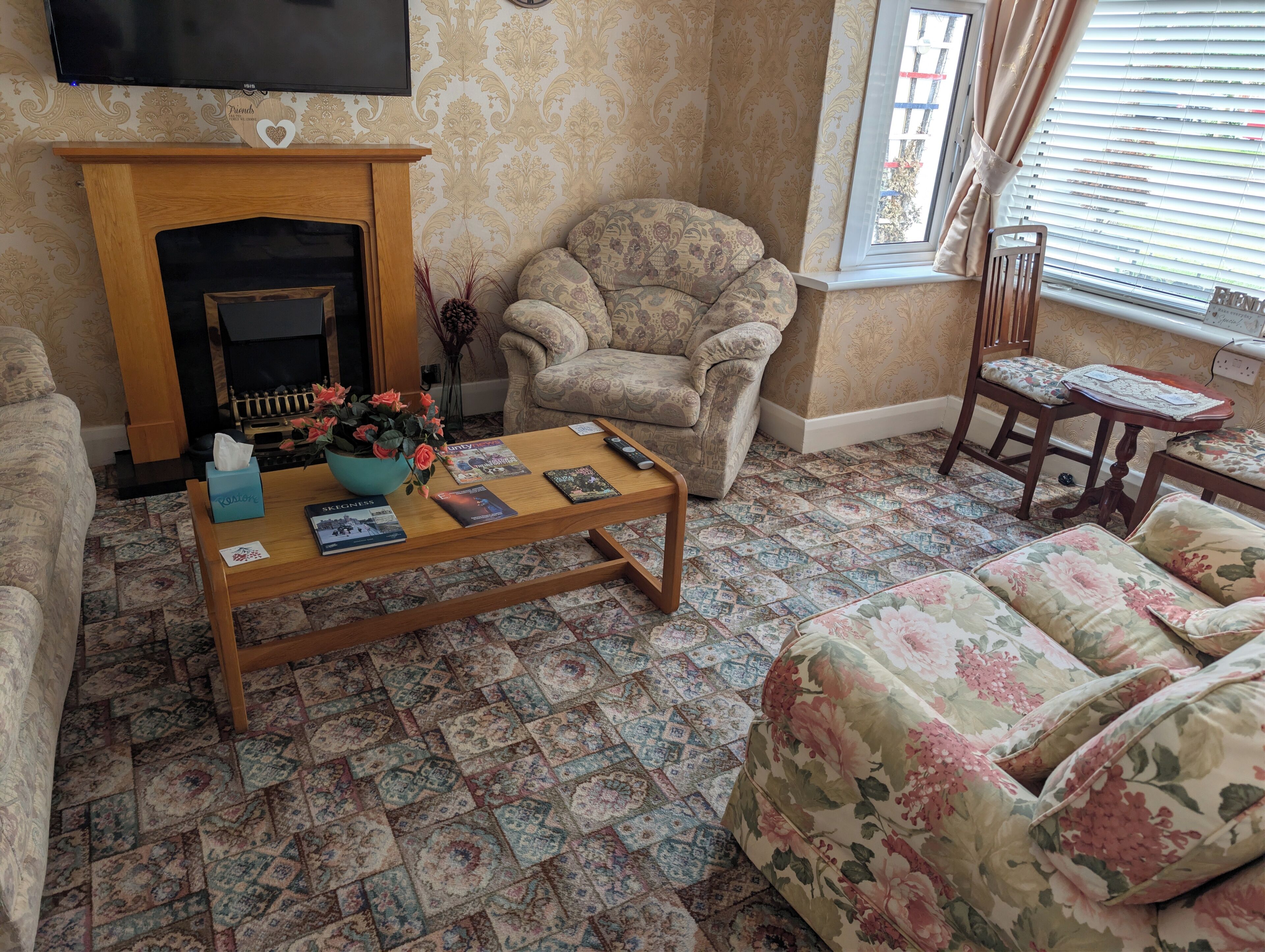 A living room with a fireplace, patterned carpet, floral sofa, and a coffee table with books.