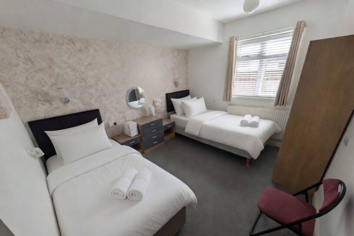 A hotel room with two beds, a desk, a chair, a mirror, and a window with curtains.