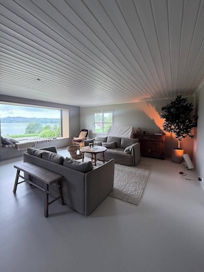 A modern living room with a large window, a sofa set, a coffee table, and a potted plant. - Family home with fairytale garden in Talgje (Rogaland)