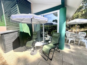 Eine Terrasse im Freien mit Grill, zwei grünen Lounge-Stühlen, einem Tisch und einem gestreiften Sonnenschirm.
