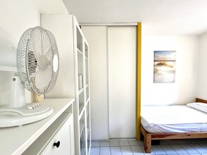 Ein Schlafzimmer mit einem Bett, einem weißen Kleiderschrank, einem Nachttisch mit Ventilator und einem Bild an der Wand.