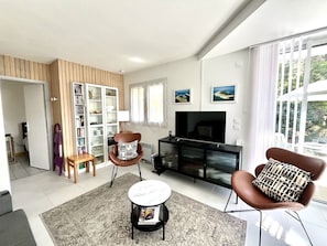 Ein modernes Wohnzimmer mit Kamin, Fernseher, Bücherregal und Essbereich mit Tisch und Stühlen.