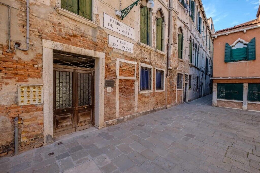 Un vicolo stretto con edifici storici, un cancello in metallo e un cartello che indica 'Campo do Pozzi'.