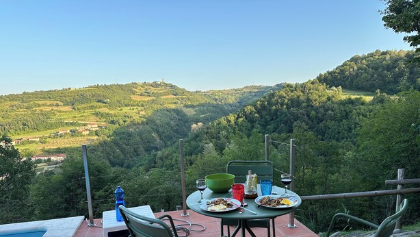 A terrace with a table set for dining, chairs, a pool, and a view of a forested valley. - Peaceful Holiday House with Private Pool and Panoramic Views: Casa Mumu (Casteletto D’Erro)