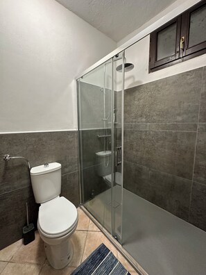 A bathroom with a toilet, a shower with a glass door, and a tiled wall. - Peaceful Holiday House with Private Pool and Panoramic Views: Casa Mumu (Casteletto D’Erro)