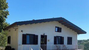 A two-story building with a stone-paved entrance, a balcony with a railing, and a small garden area. - Peaceful Holiday House with Private Pool and Panoramic Views: Casa Mumu (Casteletto D’Erro)