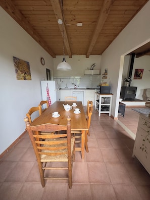 Un comedor con una mesa y sillas de madera, una cocina al fondo y una chimenea.