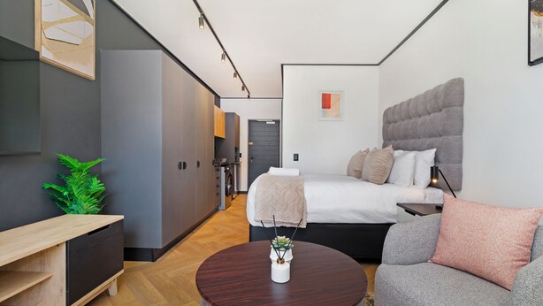 Une chambre d’hôtel moderne comprenant un lit, un canapé, une petite table, une plante et un coin cuisine.