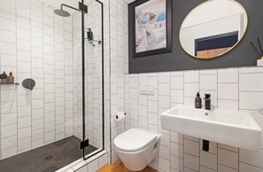 A bathroom with a shower, toilet, sink, and a framed picture on the wall. - Modern Studio | Nine Palms Century City (Cape Town)