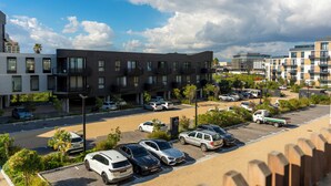 Un bâtiment moderne à plusieurs étages, un parking avec plusieurs voitures et un ciel dégagé avec quelques nuages.