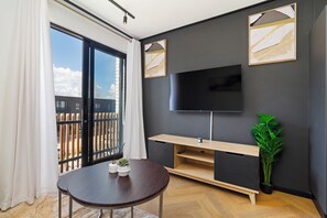A modern living room with a large TV, wooden entertainment unit, and a balcony with a view. - Modern Studio | Nine Palms Century City (Cape Town)