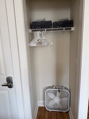 Ein Schrank mit Regalen, einem weißen Kleiderbügel und einem weißen Ventilator.