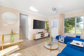 Ein modernes Wohnzimmer mit einem Glastisch, einem blauen Sofa und einem an der Wand befestigten Flachbildfernseher.