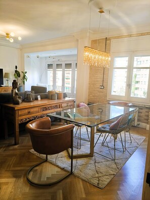 Un salon moderne avec une table à manger en verre, des fauteuils en cuir, une table basse en bois et un lustre.