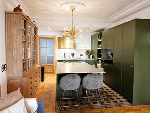 Une cuisine moderne avec un îlot central, des tabourets de bar, un meuble en bois et un luminaire décoratif au plafond.