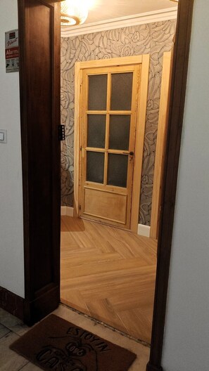 Um corredor com porta de madeira, papel de parede estampado e tapete de entrada.