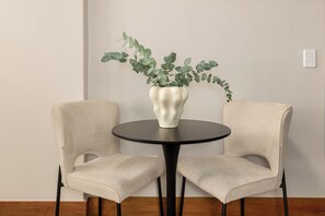 A round table with a white vase and green foliage, flanked by two beige chairs with black legs. - Charlie and the Chairman | Modern CBD Studio (Cape Town)