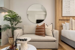 A modern living room with a sofa, a round mirror, a potted plant, and a small table with decorative items. - Charlie and the Chairman | Modern CBD Studio (Cape Town)