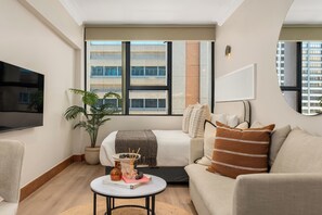 A modern living room with a large window, a flat-screen TV, a sofa, a coffee table, and a potted plant. - Charlie and the Chairman | Stylish Studio (Cape Town)