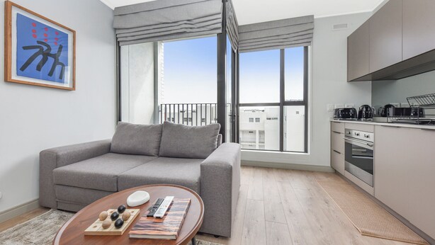 A modern living room with a grey sofa, a wooden coffee table, and a view of a cityscape through large windows. - One Rosebank | Slow Luxury, Perfected (Johannesburg)