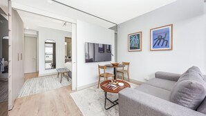 A modern living room with a grey sofa, a coffee table, and a TV mounted on the wall. There are two framed artworks on the wall. - One Rosebank | Slow Luxury, Perfected (Johannesburg)