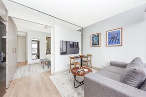 A modern living room with a grey sofa, a coffee table, and a TV mounted on the wall. There are two framed artworks on the wall. - One Rosebank | Slow Luxury, Perfected (Johannesburg)