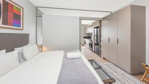 A modern hotel room with a bed, a desk, a chair, and a view into the kitchen area. - One Rosebank | Slow Luxury, Perfected (Johannesburg)