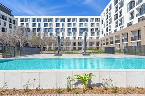 Ein modernes Apartmenthaus mit Schwimmbad, umgeben von einer Hecke und Bäumen.