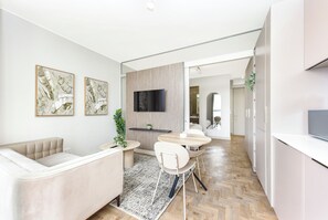 Eine moderne Küche mit weißen Schränken, ein Essbereich mit rundem Tisch und Stühlen, eine Sitzecke und ein an der Wand befestigtes Fernsehgerät.
