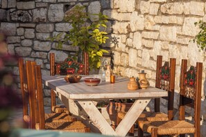 A rustic outdoor dining area with a stone wall backdrop, wooden table, wicker chairs, and decorative items. - Perfect Escape Luxurious Villa Anastasia Tranquil Retreat in Arkadades Greece (Corfu)