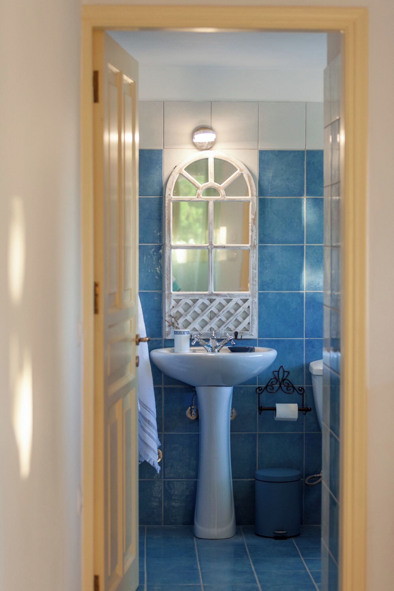 A bathroom with a pedestal sink, a window with a decorative grille, and blue tiles.