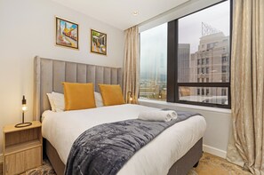 Ein Hotelzimmer mit einem großen Bett, einem Nachttisch, einem Fenster mit Vorhängen und zwei gerahmten Bildern an der Wand.